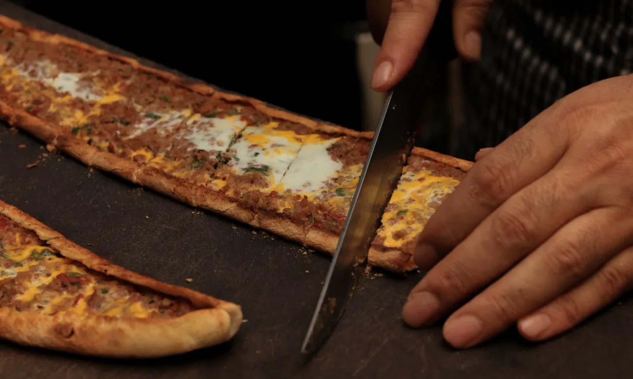 Fırından yeni çıkan kıymalı yumurtalı pide tezgâhta dilimleniyor